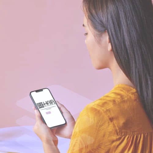 Woman in yellow top using smartphone with text visible on the screen about an Omaha beauty hair salon.