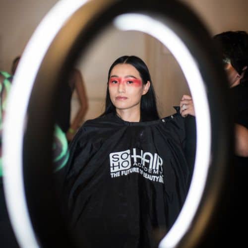 A person getting their hair styled at a beauty salon, viewed through a circular lighting ring.