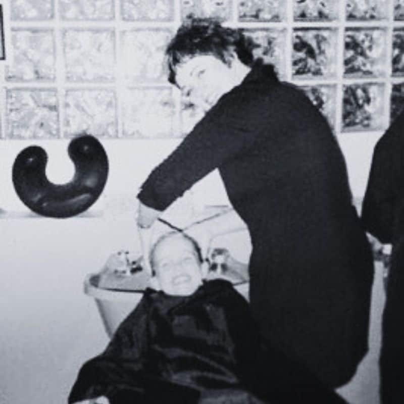 A woman appears to be laughing while styling another person's hair in a beauty salon.