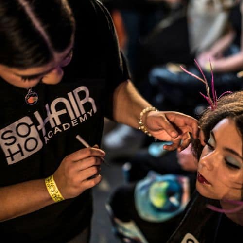 A hairstylist from a hair salon applying makeup to a woman at an event.