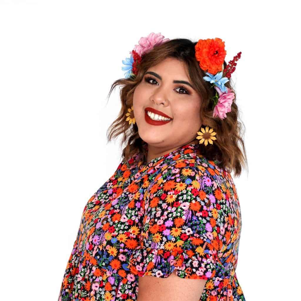 Woman smiling with a floral headband and a colorful floral blouse against a white background, perfectly styled at a beauty salon.