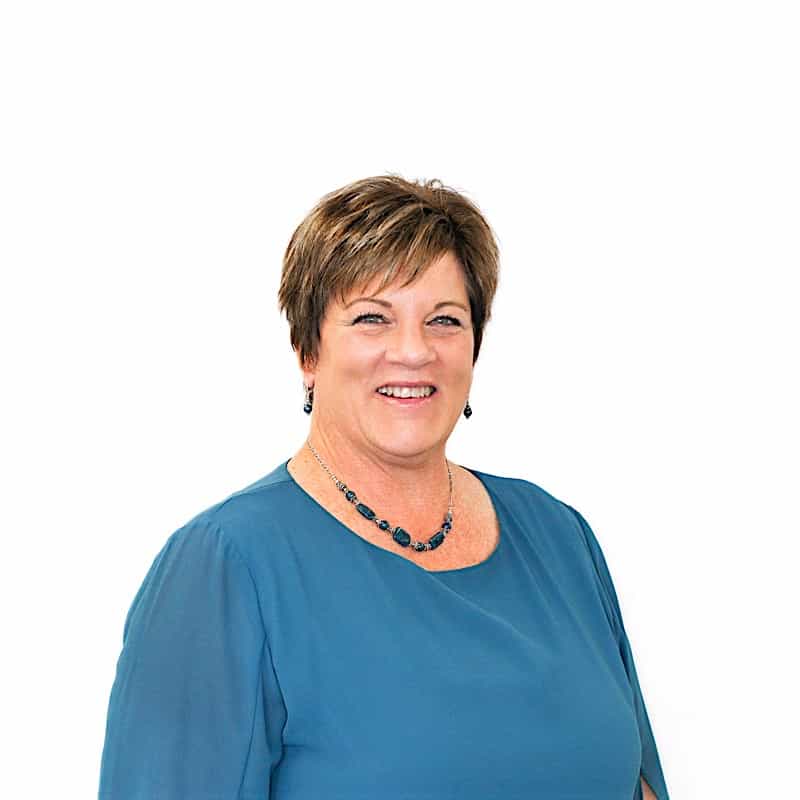 A smiling woman with short hair, fresh from a beauty salon in Omaha, wearing a blue top and a necklace, against a white background.
