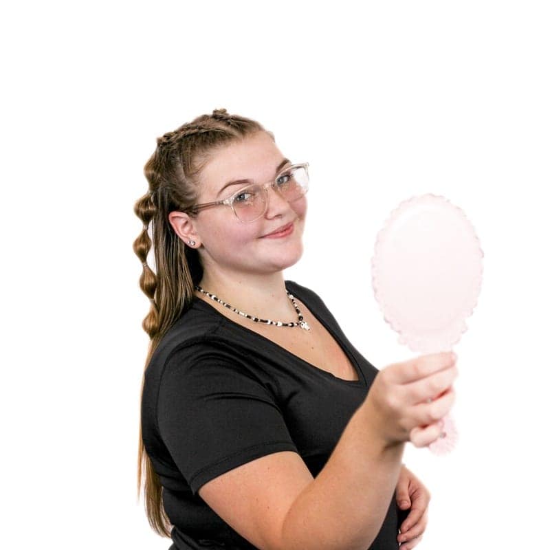 Woman with glasses smiling and holding a handheld mirror at a hair salon.