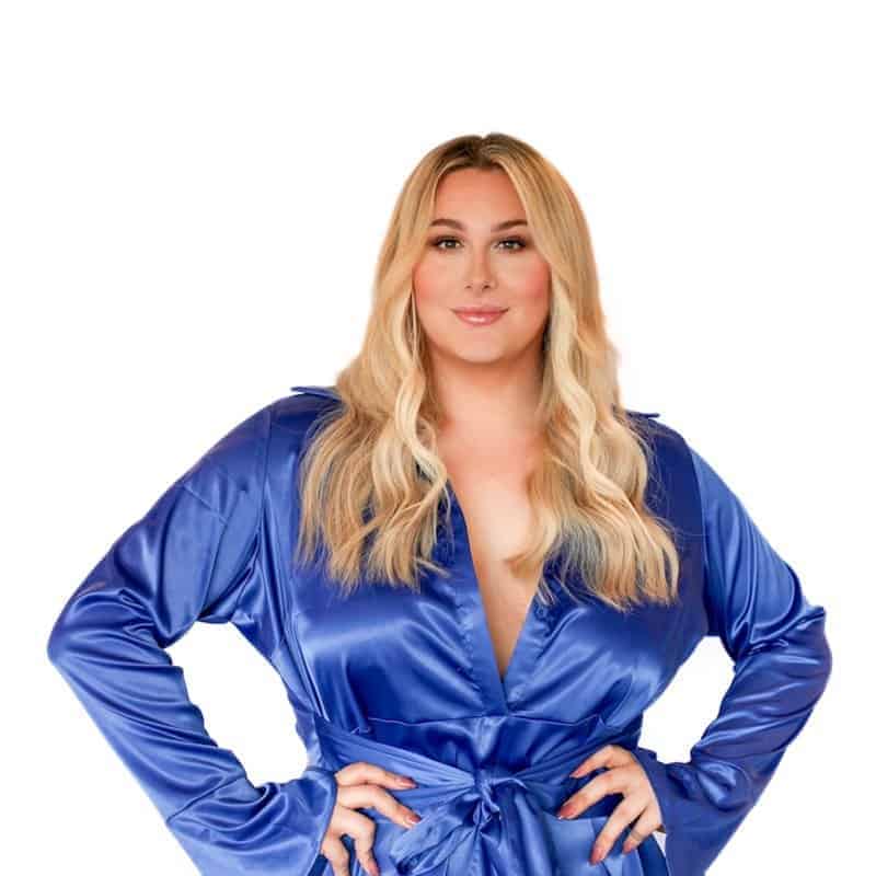 Woman in a blue dress with hands on hips and beauty school-styled hair.