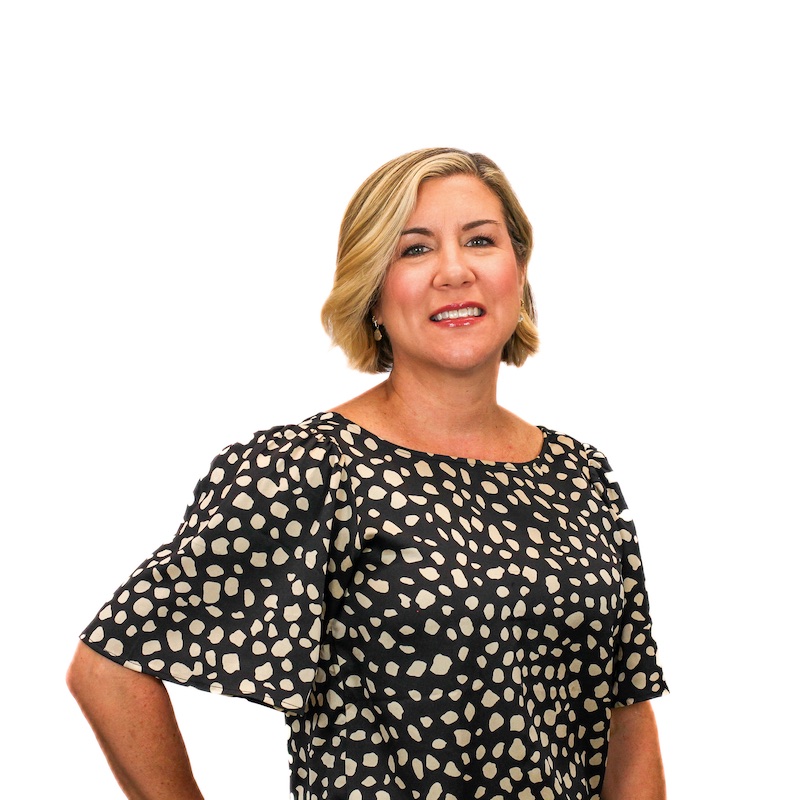 A woman with short, blonde hair stands against a white background, wearing a black and white patterned dress with short puff sleeves.