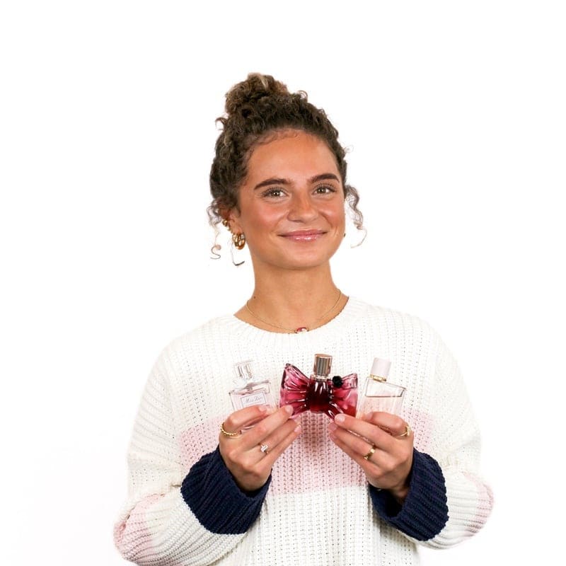 Woman holding several bottles of perfume with a pleasant expression in a cosmetology school.