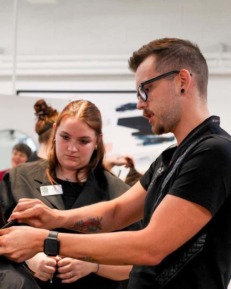 A hairstylist demonstrating a technique to an attentive trainee in a hair school setting in Omaha.
