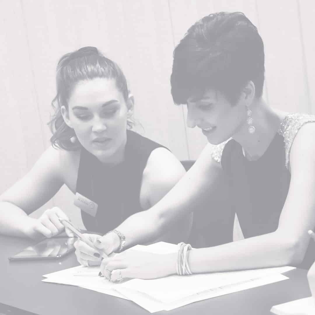 Two people seated at a table, discussing documents. One points to a paper while the other listens attentively, both focused on the task.