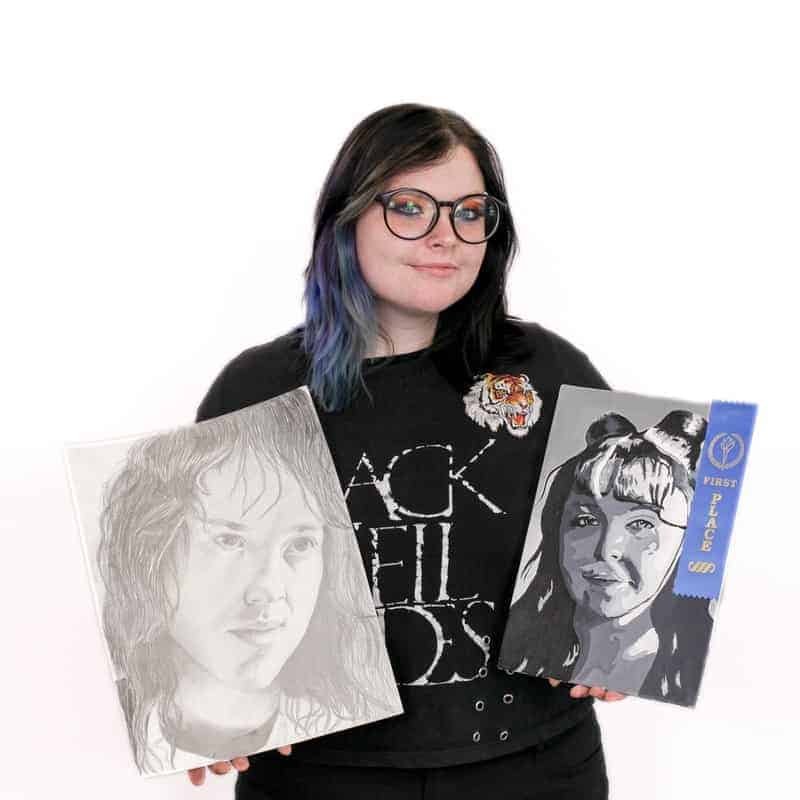 A person holding two pencil sketches of hairstyles, with one awarded a first-place ribbon from a cosmetology school.
