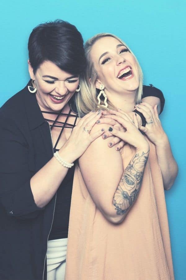 Two women sharing a joyful moment with laughter against a blue background in an Omaha beauty salon.