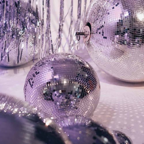 Several disco balls of varying sizes on a reflective surface, exuding beauty, with one hanging on the wall.